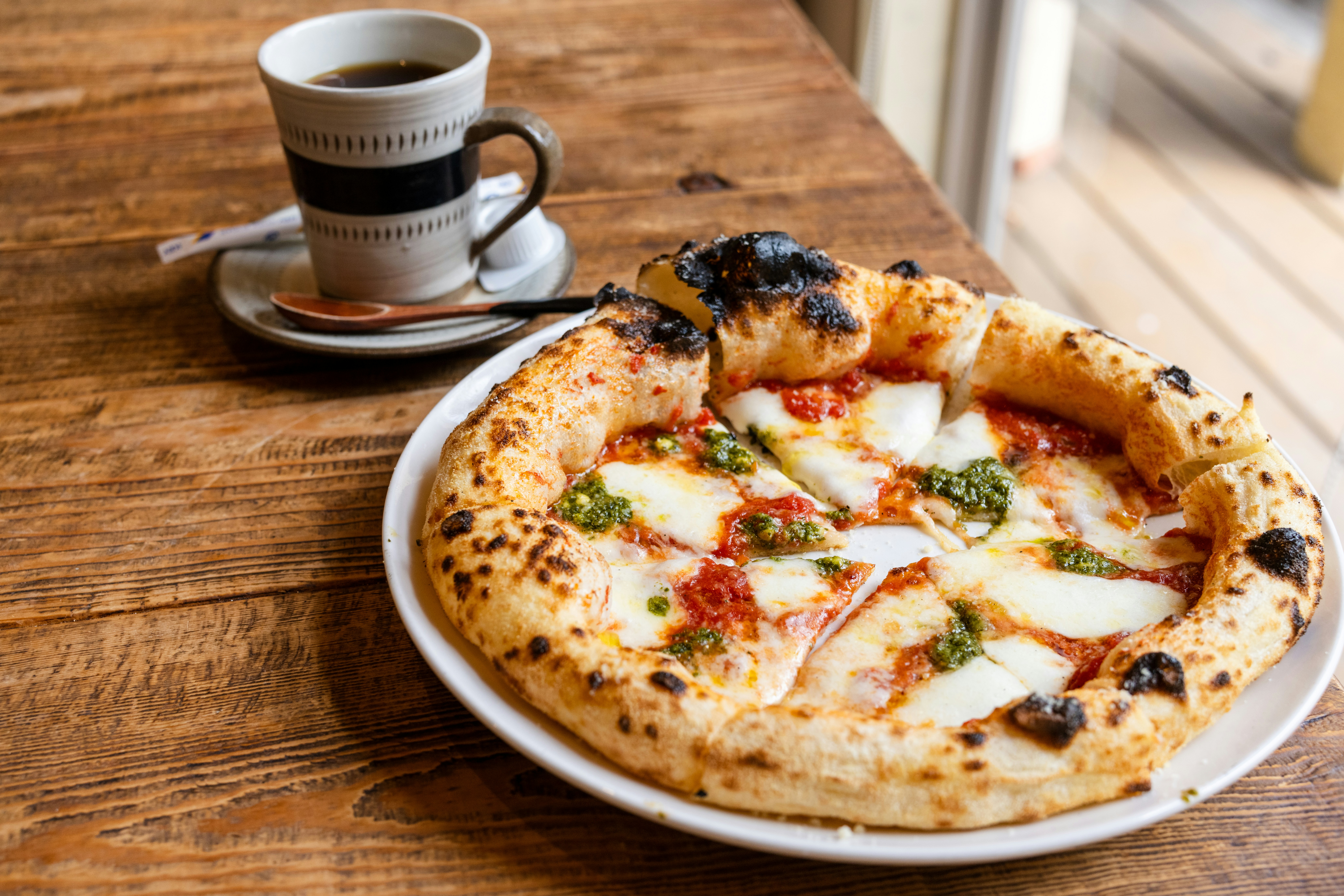 a pizza sitting on top of a white plate next to a cup of coffee