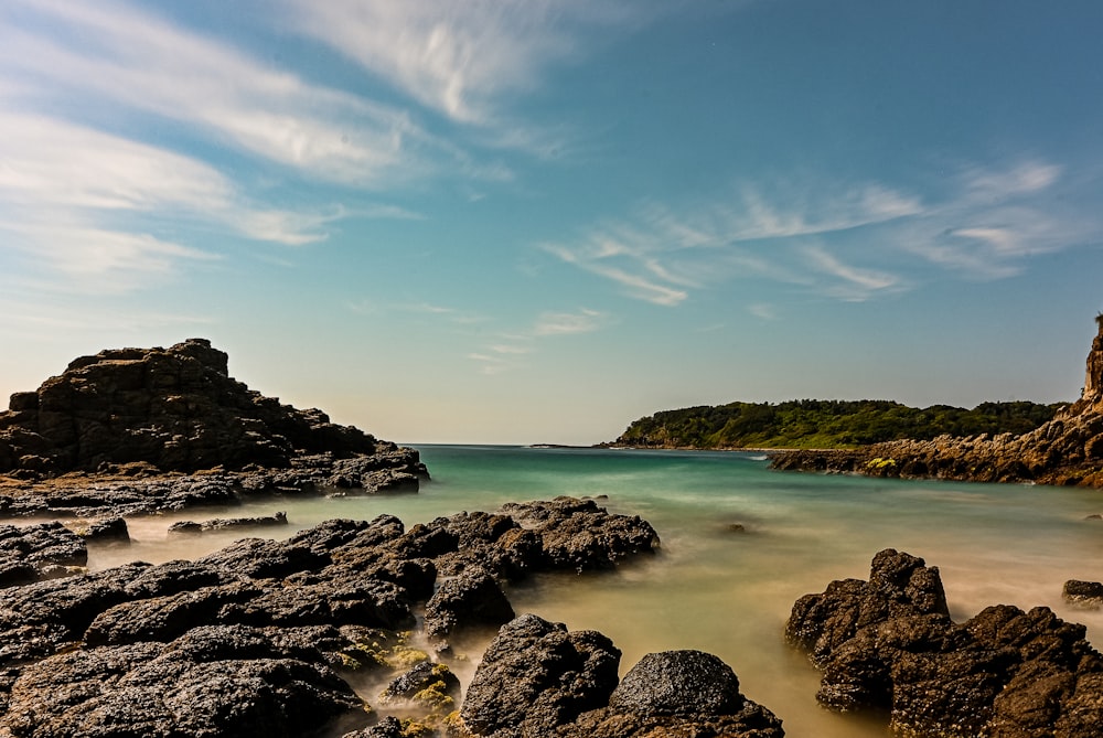 a beach with rocks and water under a blue sky