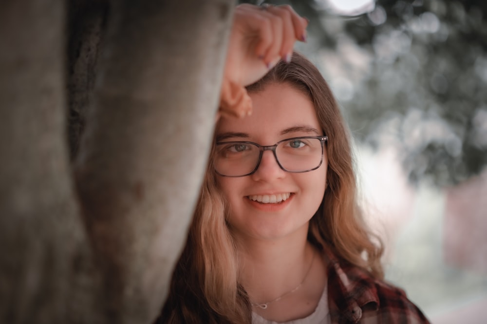 a woman wearing glasses standing next to a tree