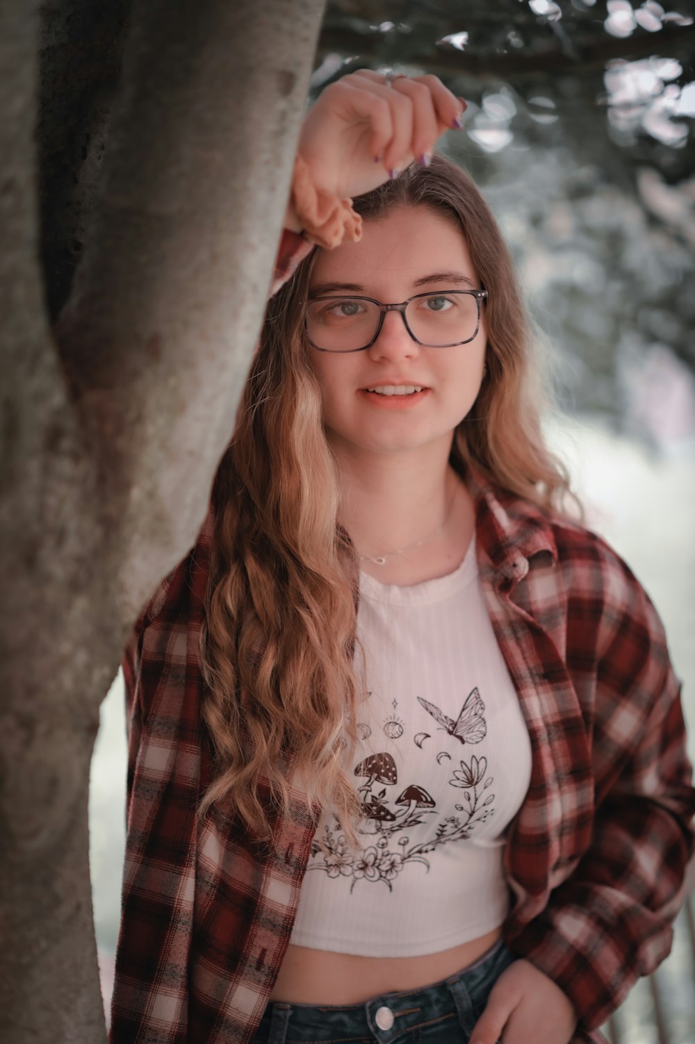 a girl wearing glasses standing next to a tree