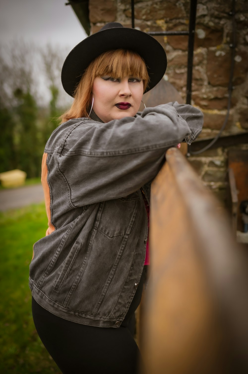 a woman in a black hat leaning on a fence