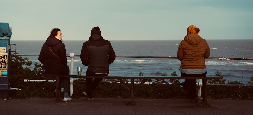 three people sitting on a bench looking at the ocean