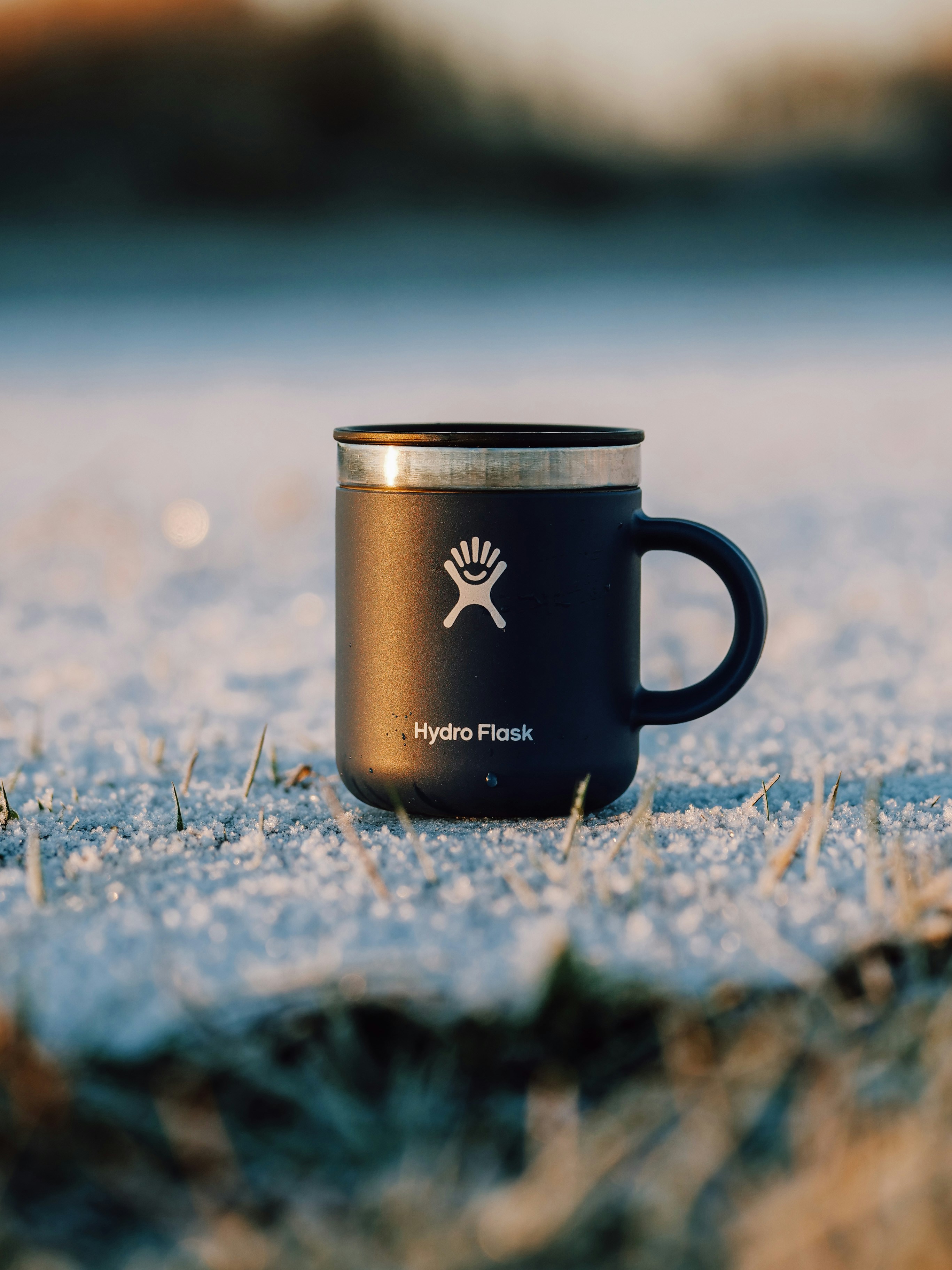 A black coffee cup sitting on top of a snow covered ground