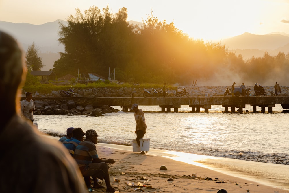 a group of people sitting on a beach next to a body of water