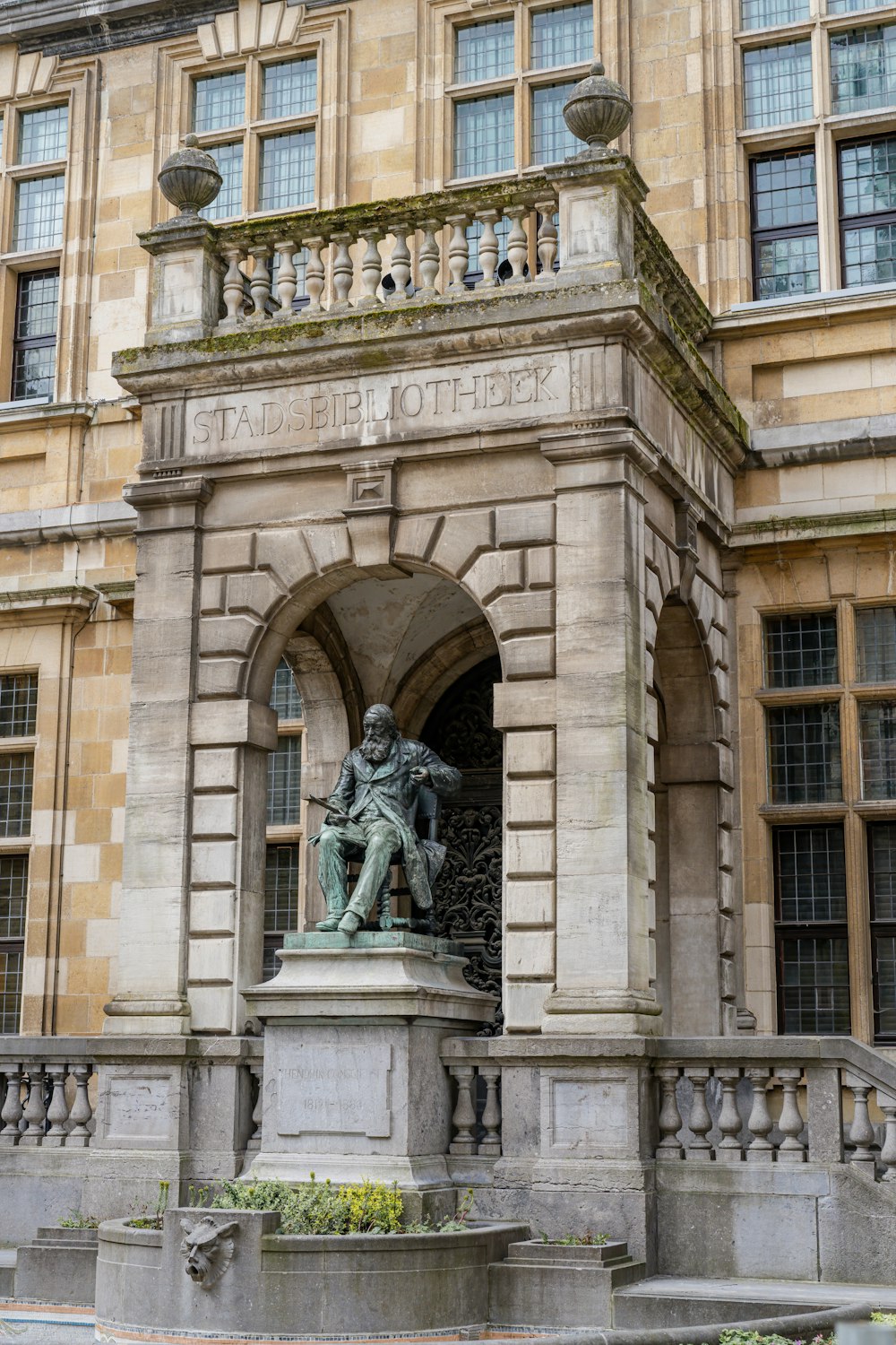 a statue of a man sitting on a bench in front of a building