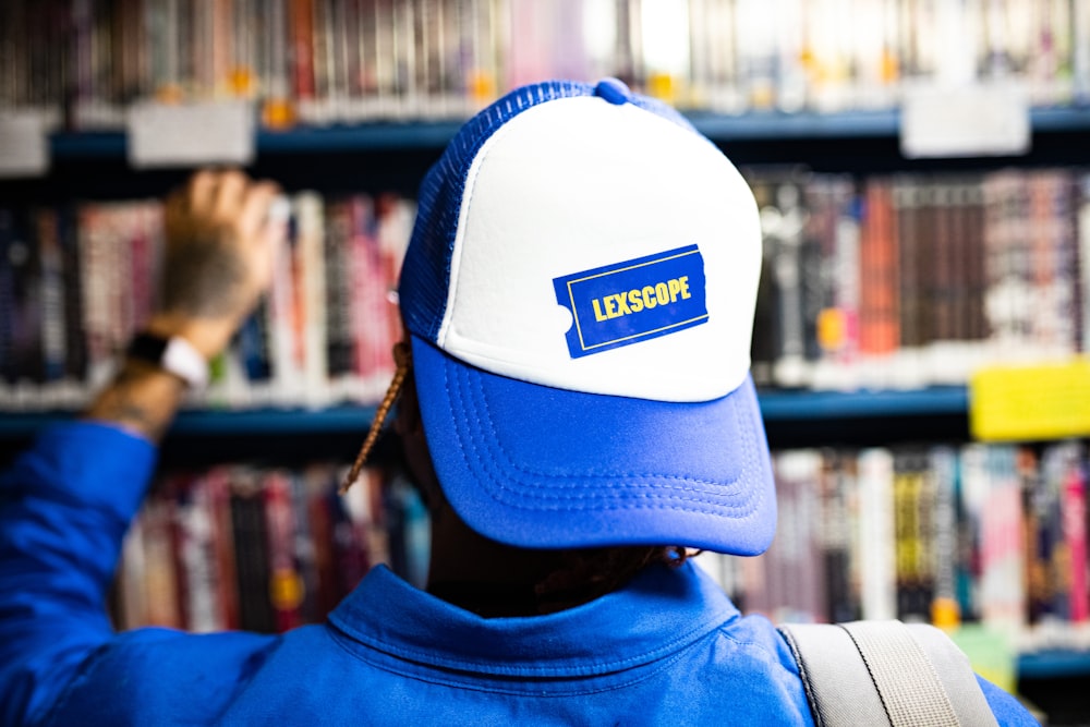 a man wearing a blue and white hat in front of a bookshelf