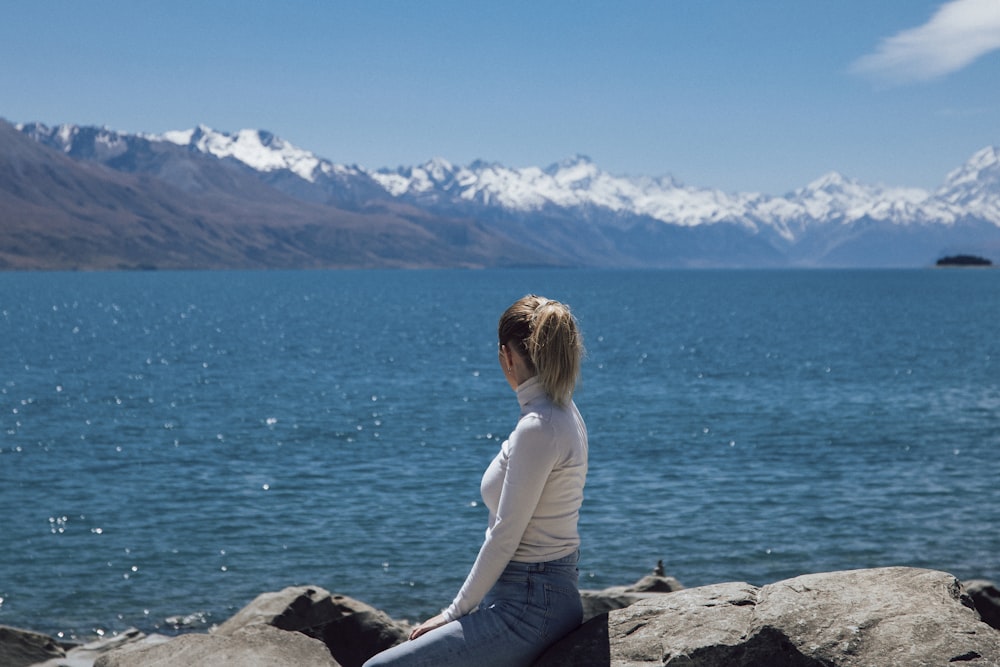 a woman is sitting on a rock by the water