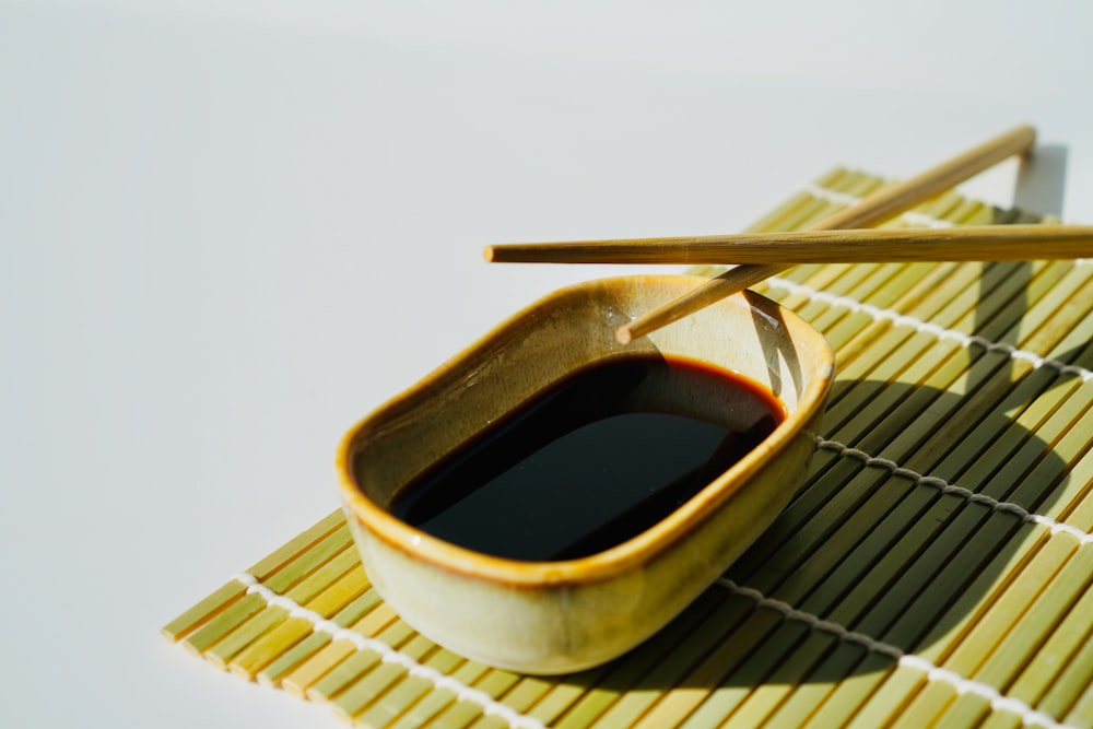 a bowl of black liquid and chopsticks on a mat