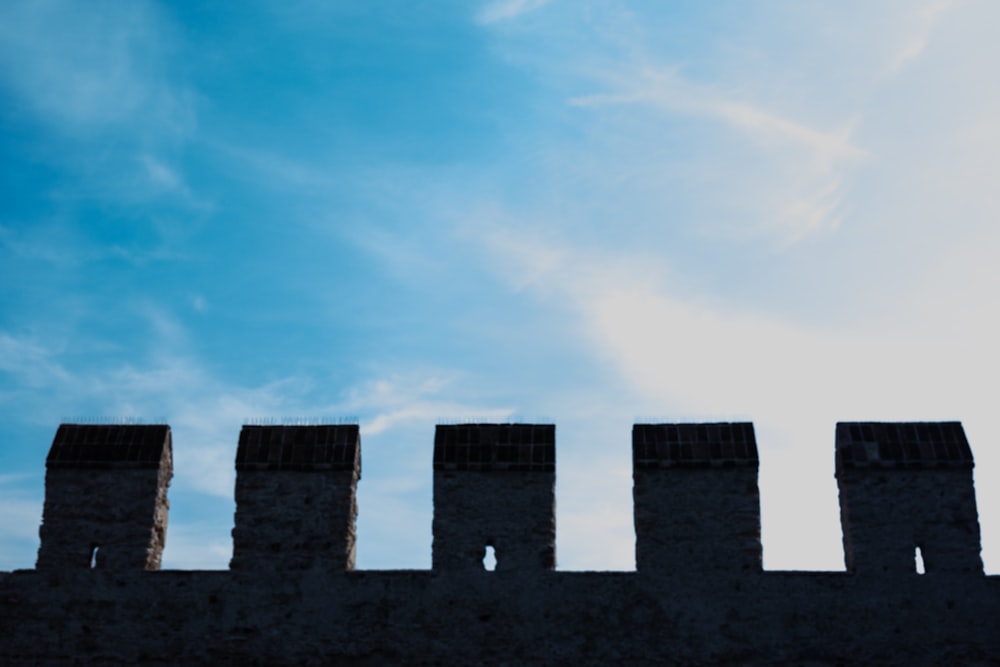 a bird flying over a stone wall under a blue sky