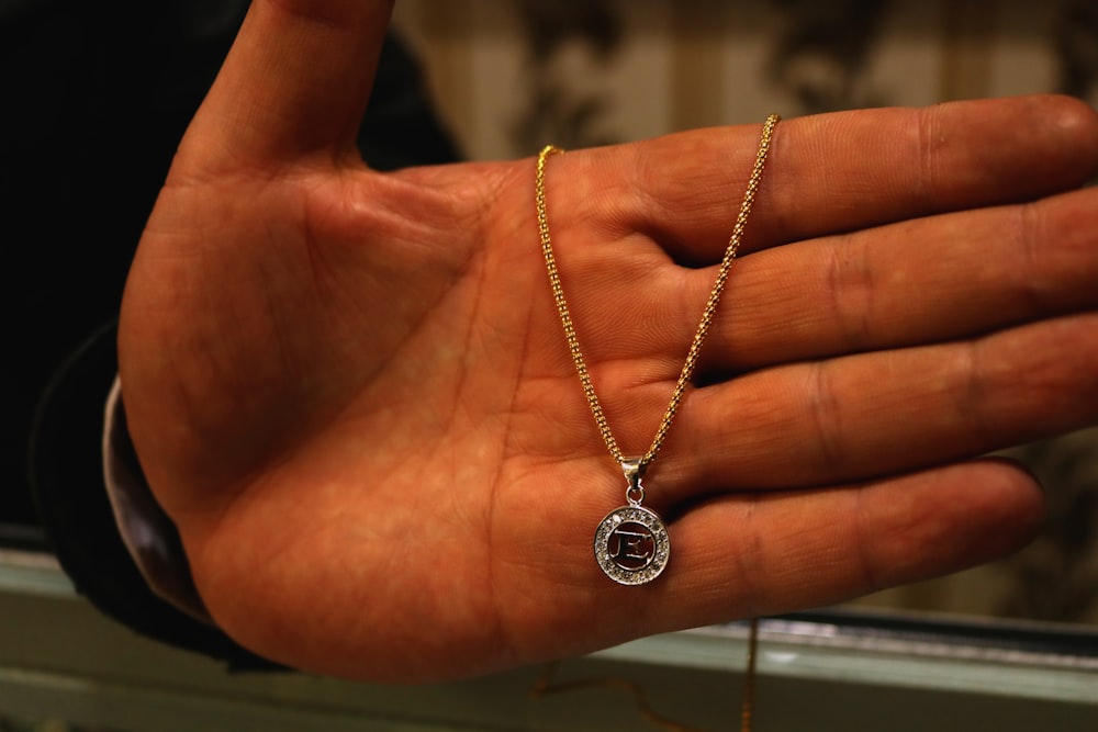a person's hand holding a gold chain with a pendant on it