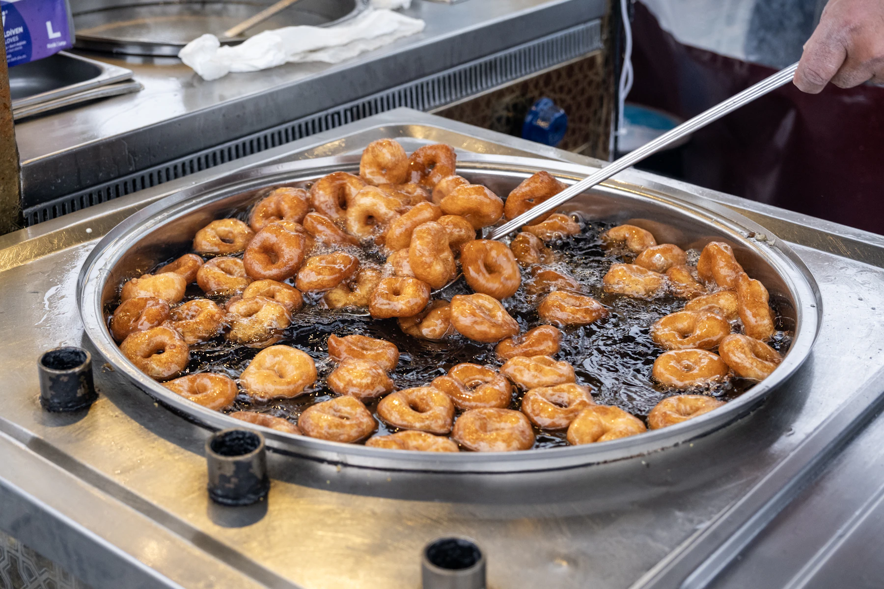 Ring donuts frying in a wide pan of oil, turned with a long-handled skimmer