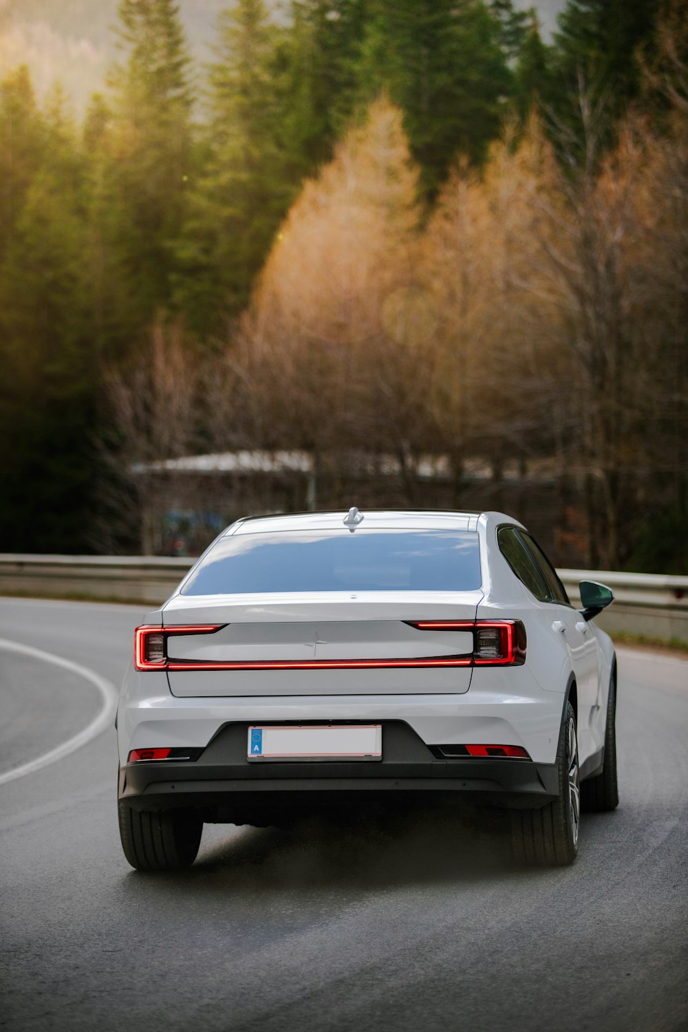 a white car driving down a road next to a forest