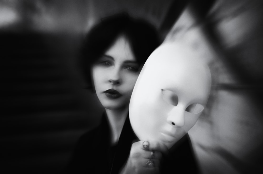a woman holding a white mask in front of her face