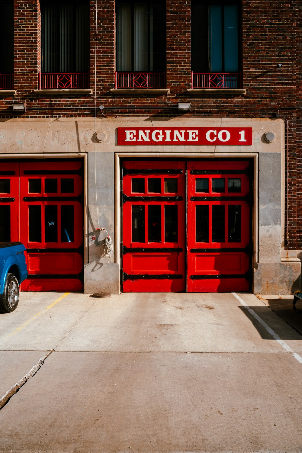 Um caminhão azul estacionado em frente a um quartel de bombeiros vermelho
