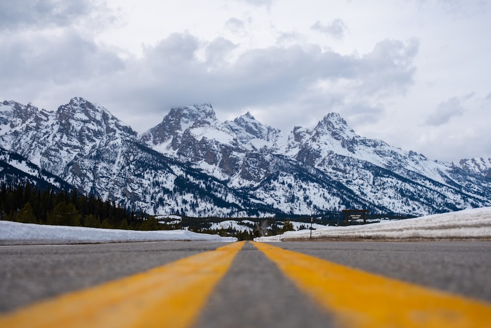 a road with a yellow line in front of a mountain range