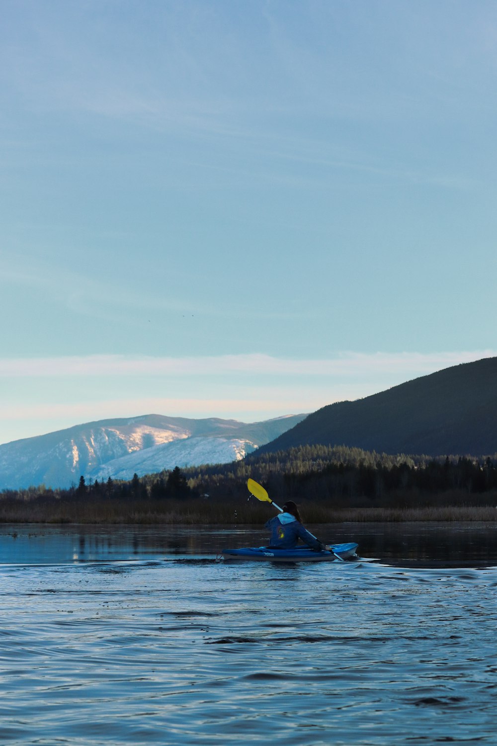 una persona en un kayak en un lago con montañas en el fondo