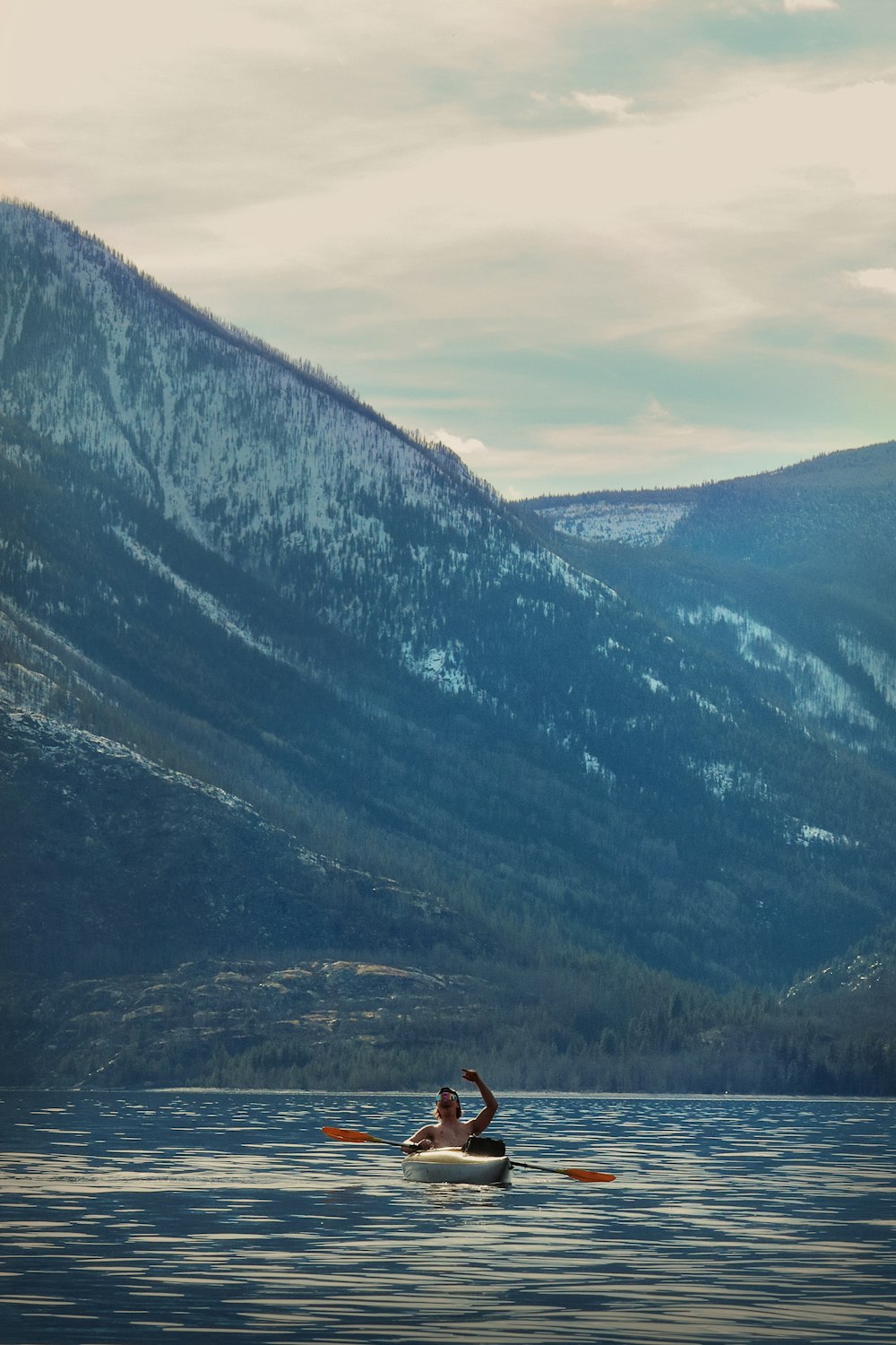 a person on a kayak in the water with mountains in the background