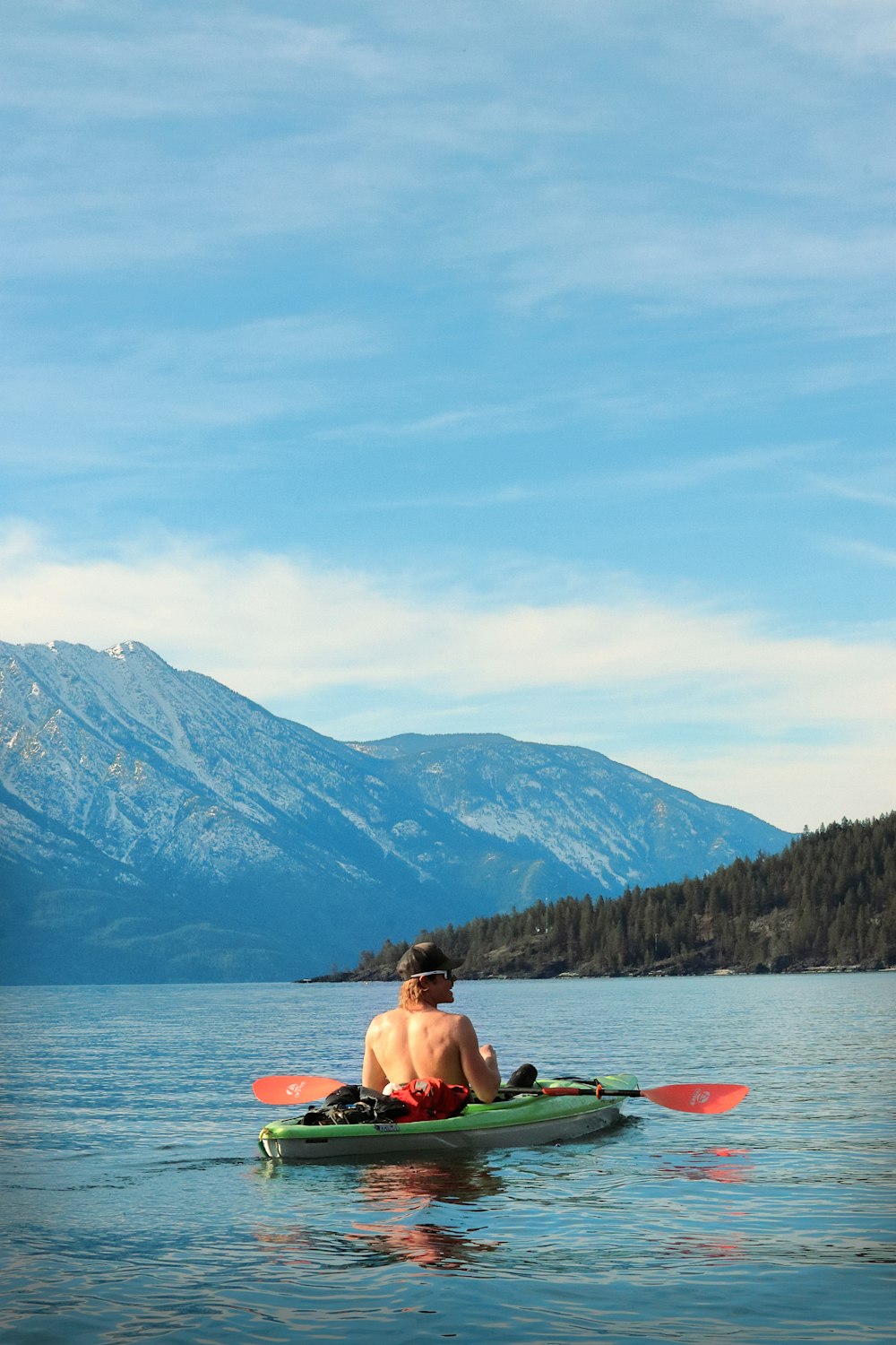 a man sitting in a kayak on a lake with mountains in the background