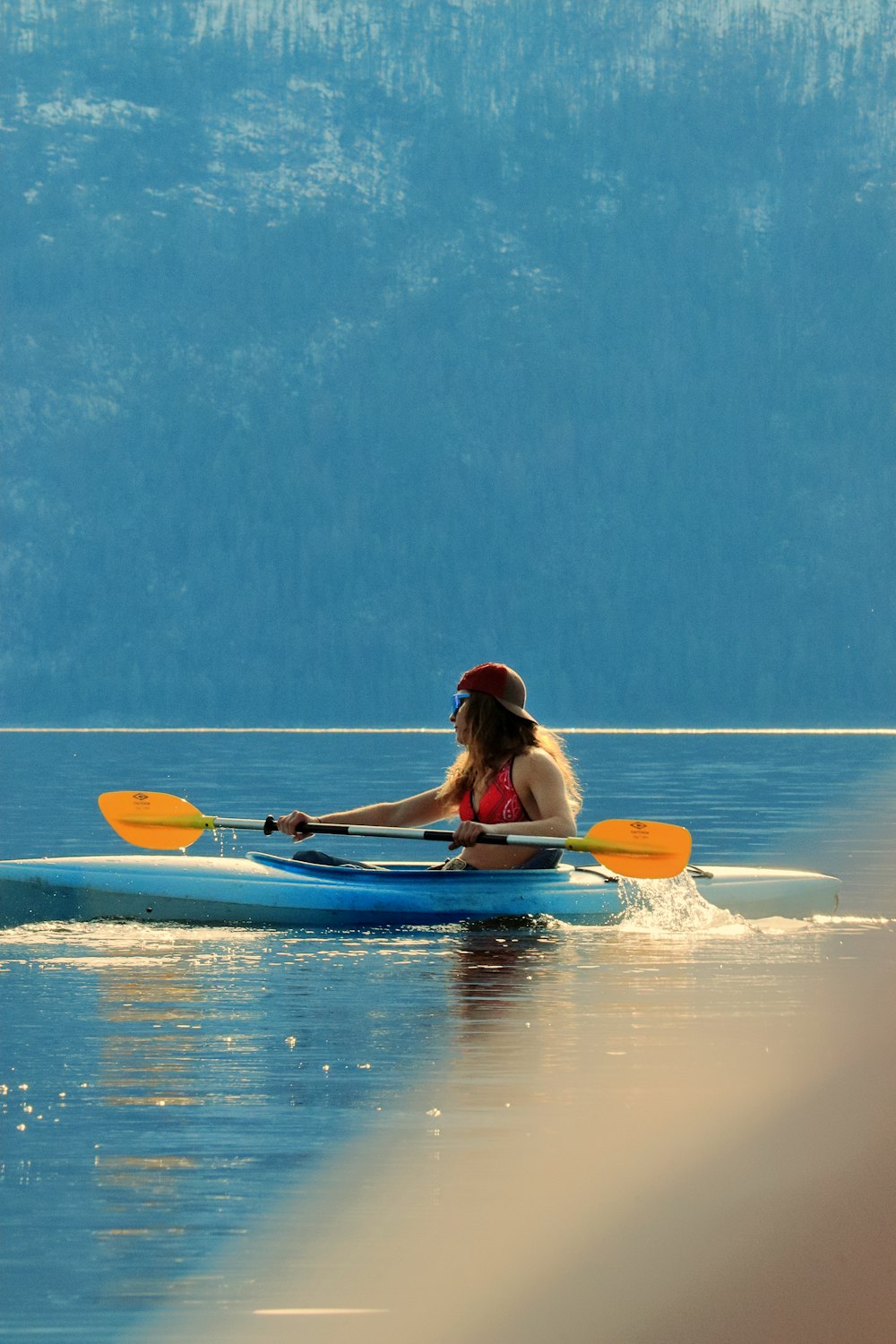 a woman in a red bikini paddling a blue kayak