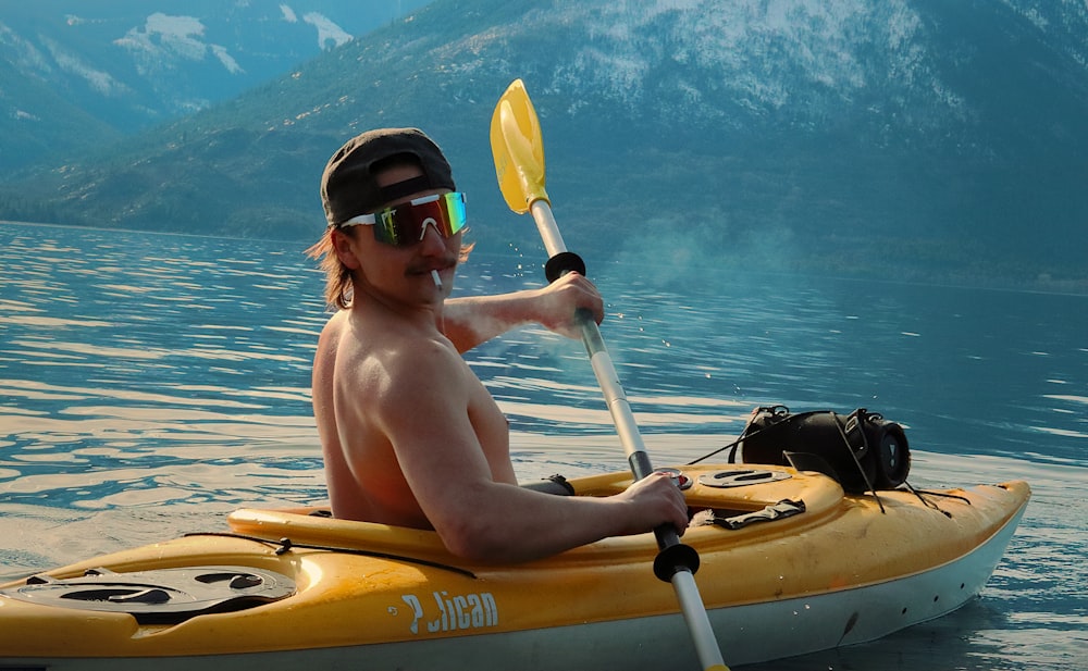a shirtless man paddling a kayak on a lake