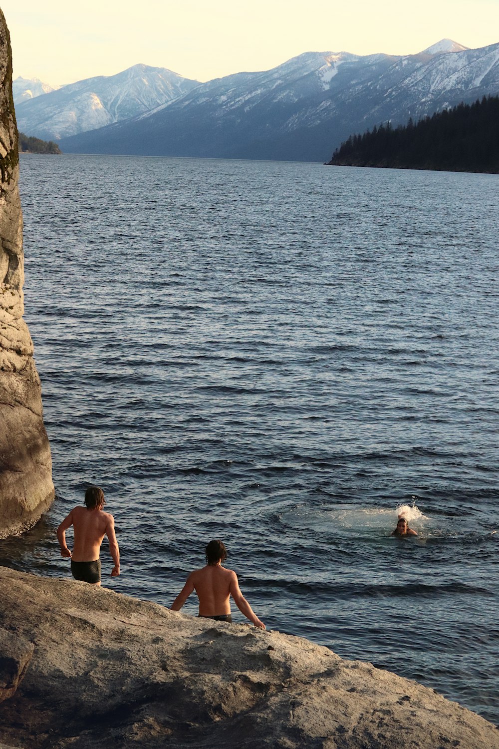 a couple of people sitting on top of a rock next to a body of water