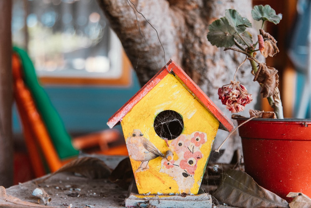 a yellow birdhouse sitting next to a potted plant