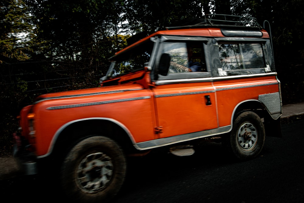 Ein orangefarbener Land Rover fährt die Straße entlang