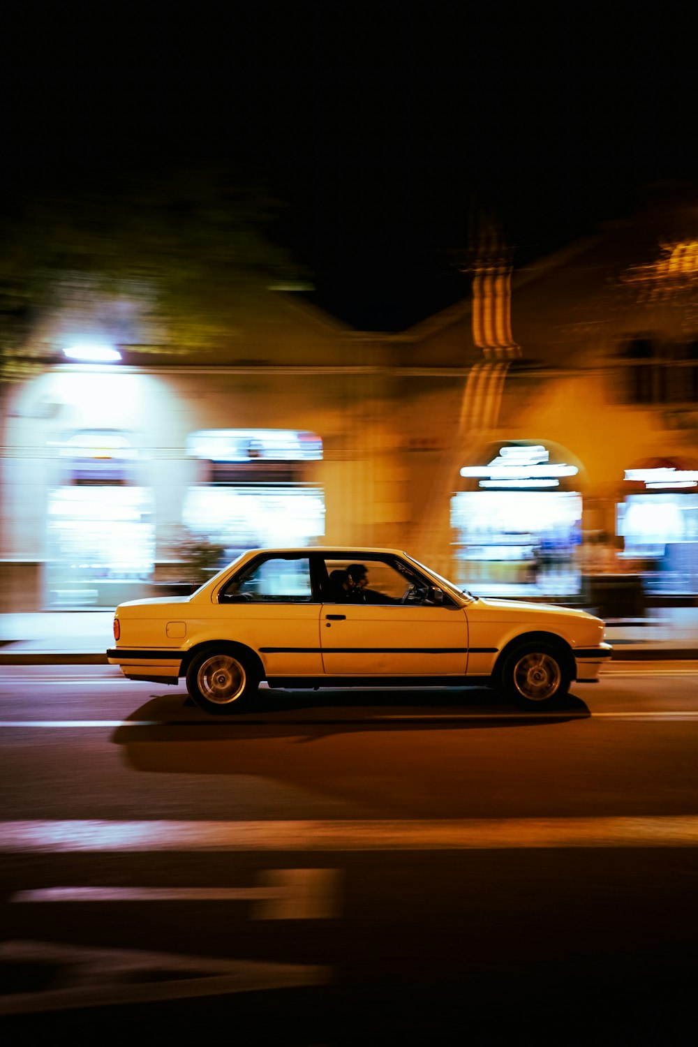 a yellow car driving down a street at night