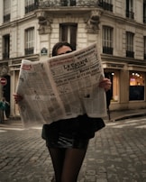 a woman walking down a street while holding a newspaper