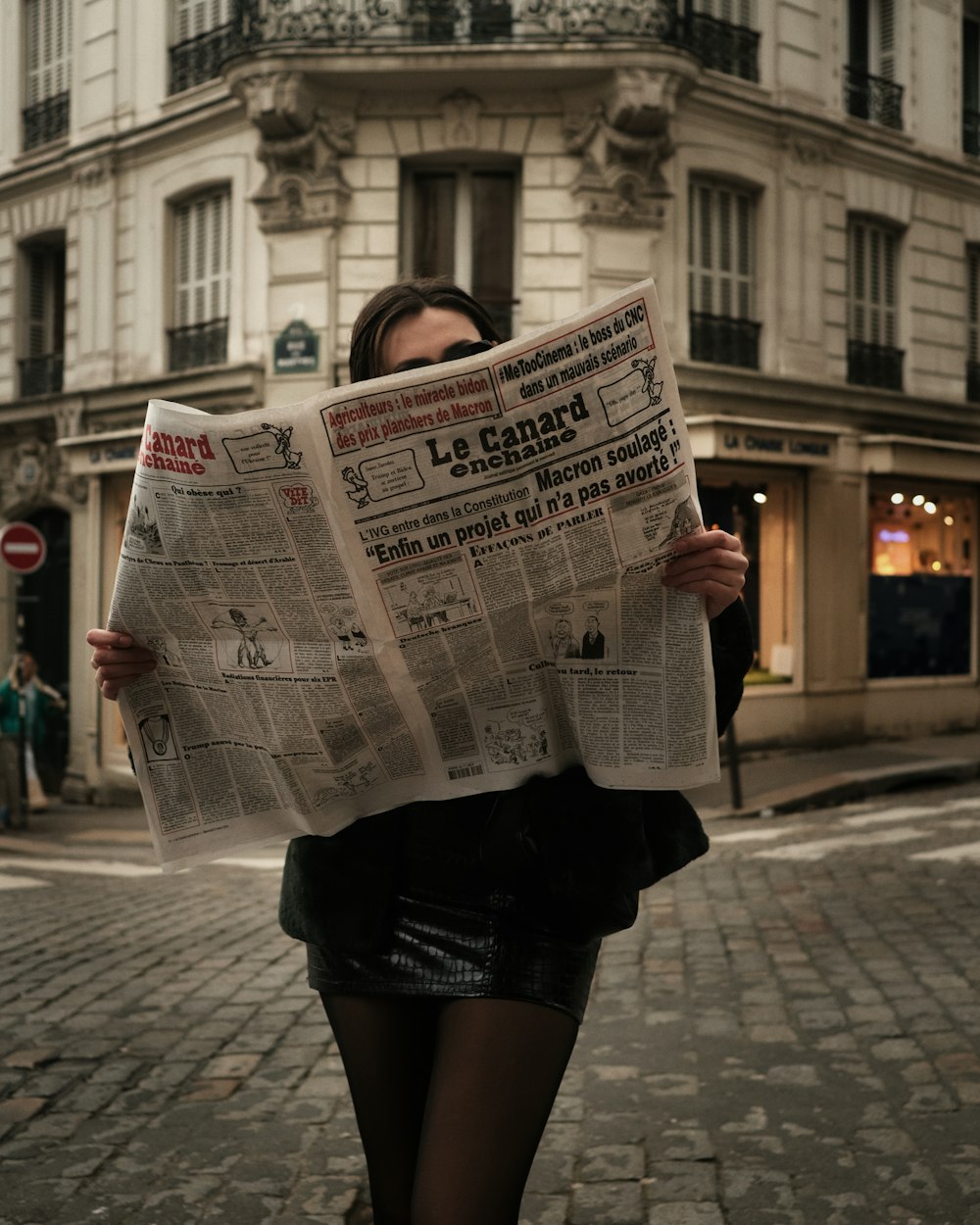 a woman walking down a street while holding a newspaper