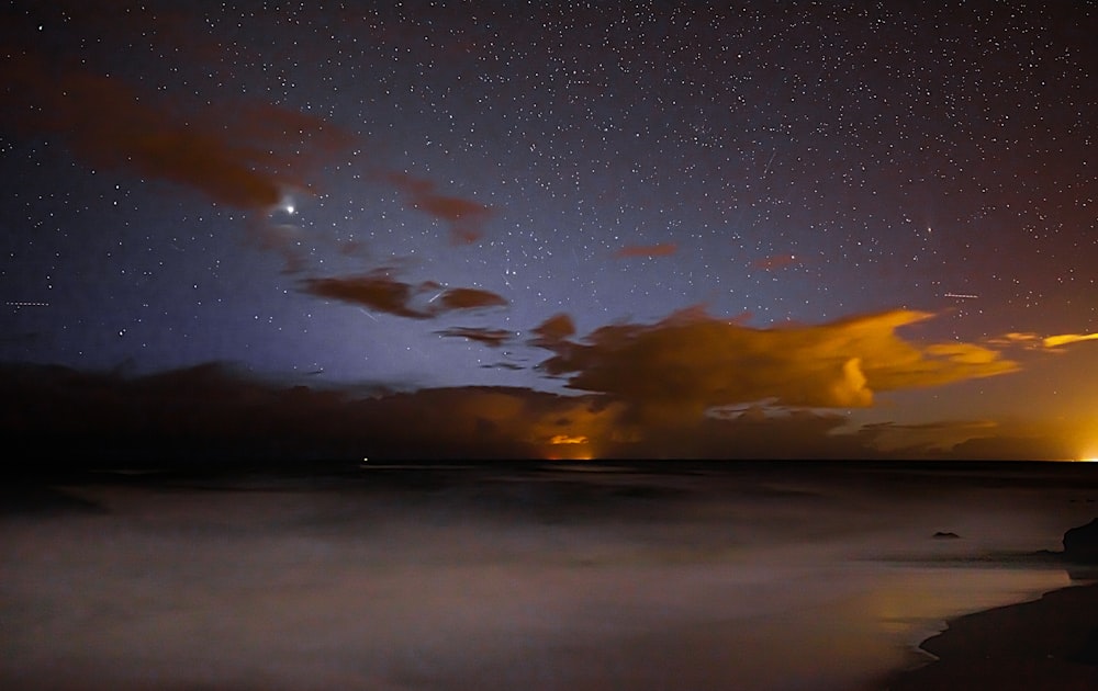 a night sky with stars and clouds over a body of water