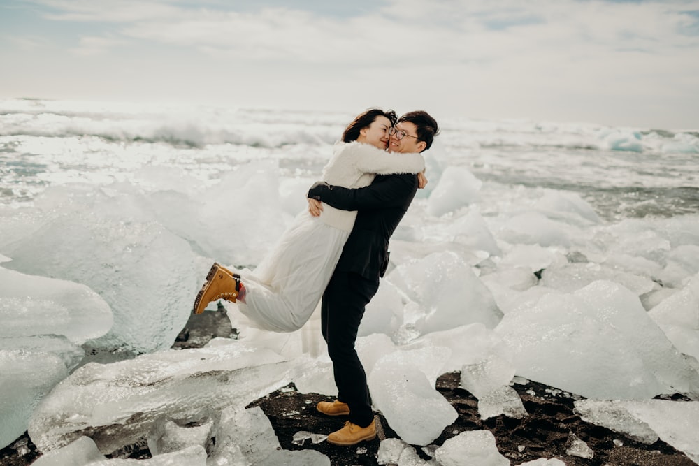 a bride and groom kissing on a rocky beach covered in ice