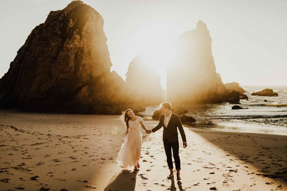 a bride and groom walking on the beach holding hands