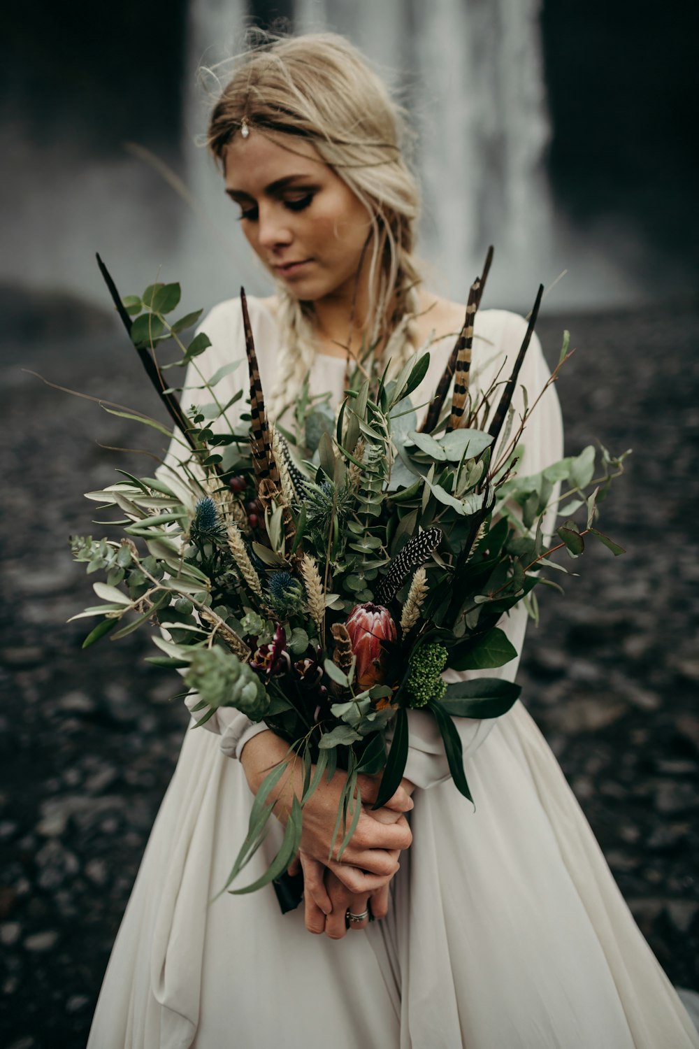 a woman holding a bouquet of flowers in front of a waterfall