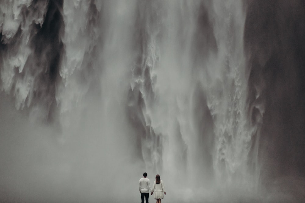 a man and a woman standing in front of a waterfall