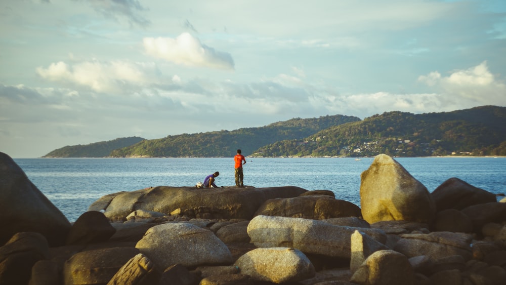 two people standing on rocks near the ocean