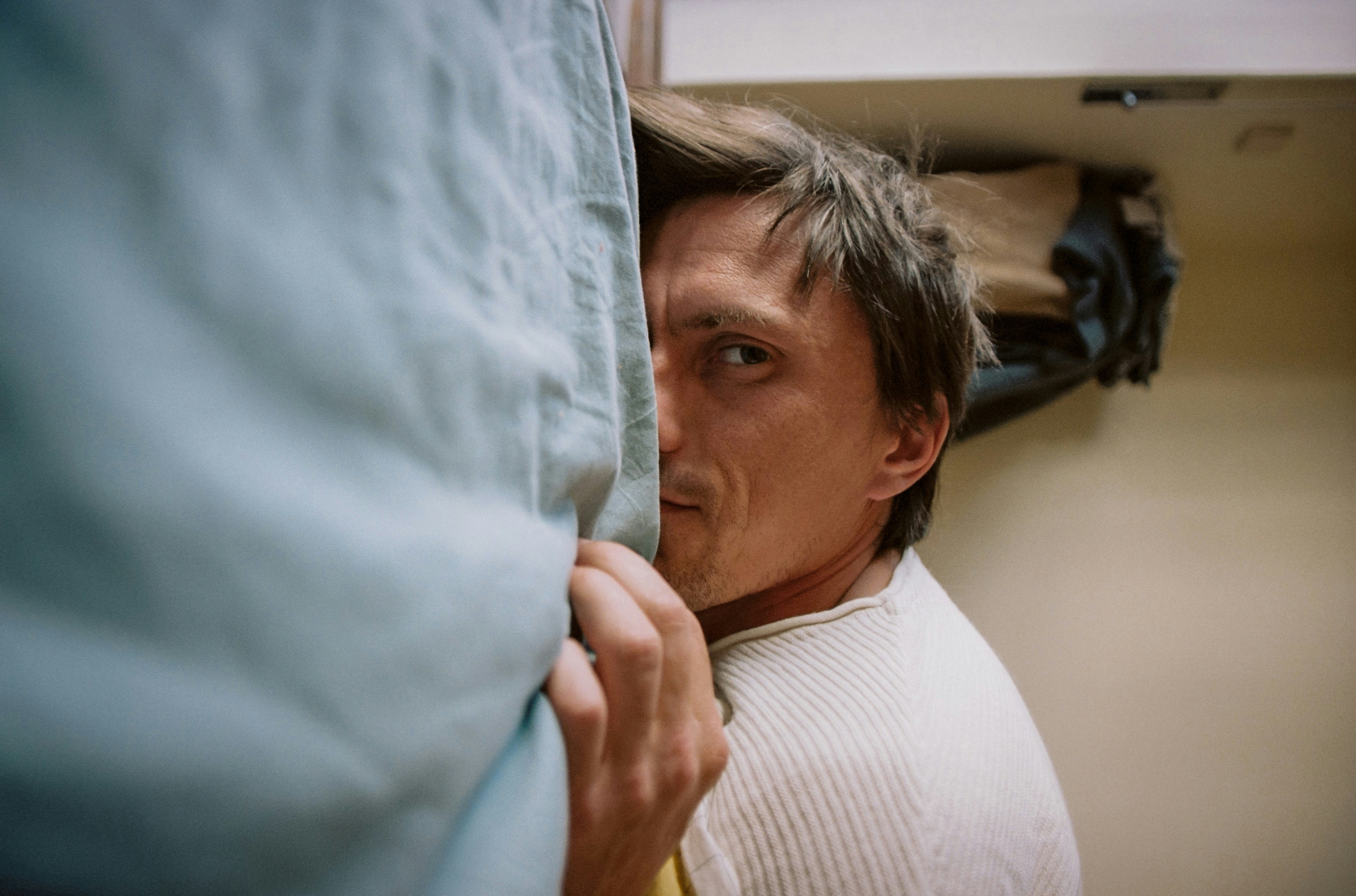 Um homem está escondido atrás de um travesseiro azul