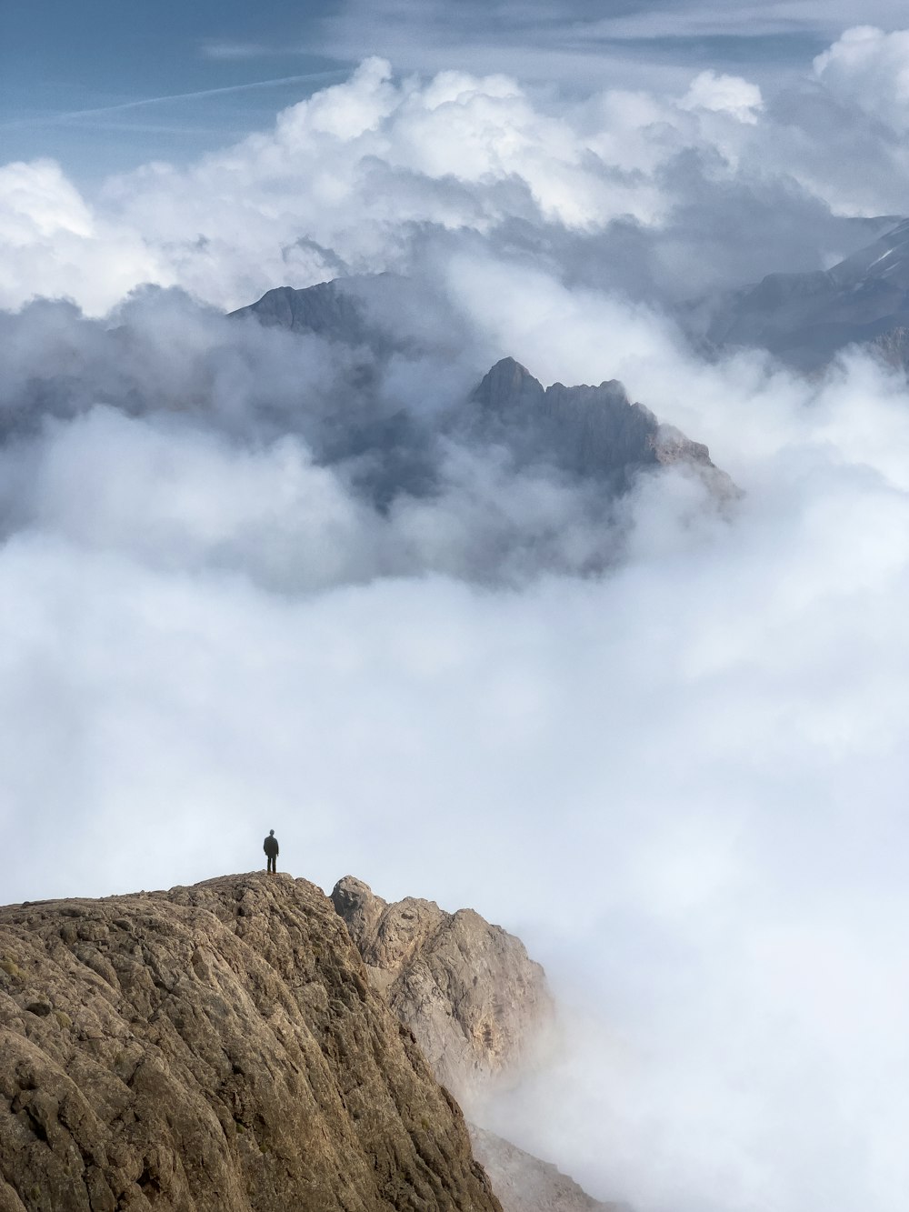 eine Person, die auf dem Gipfel eines Berges steht, der von Wolken umgeben ist