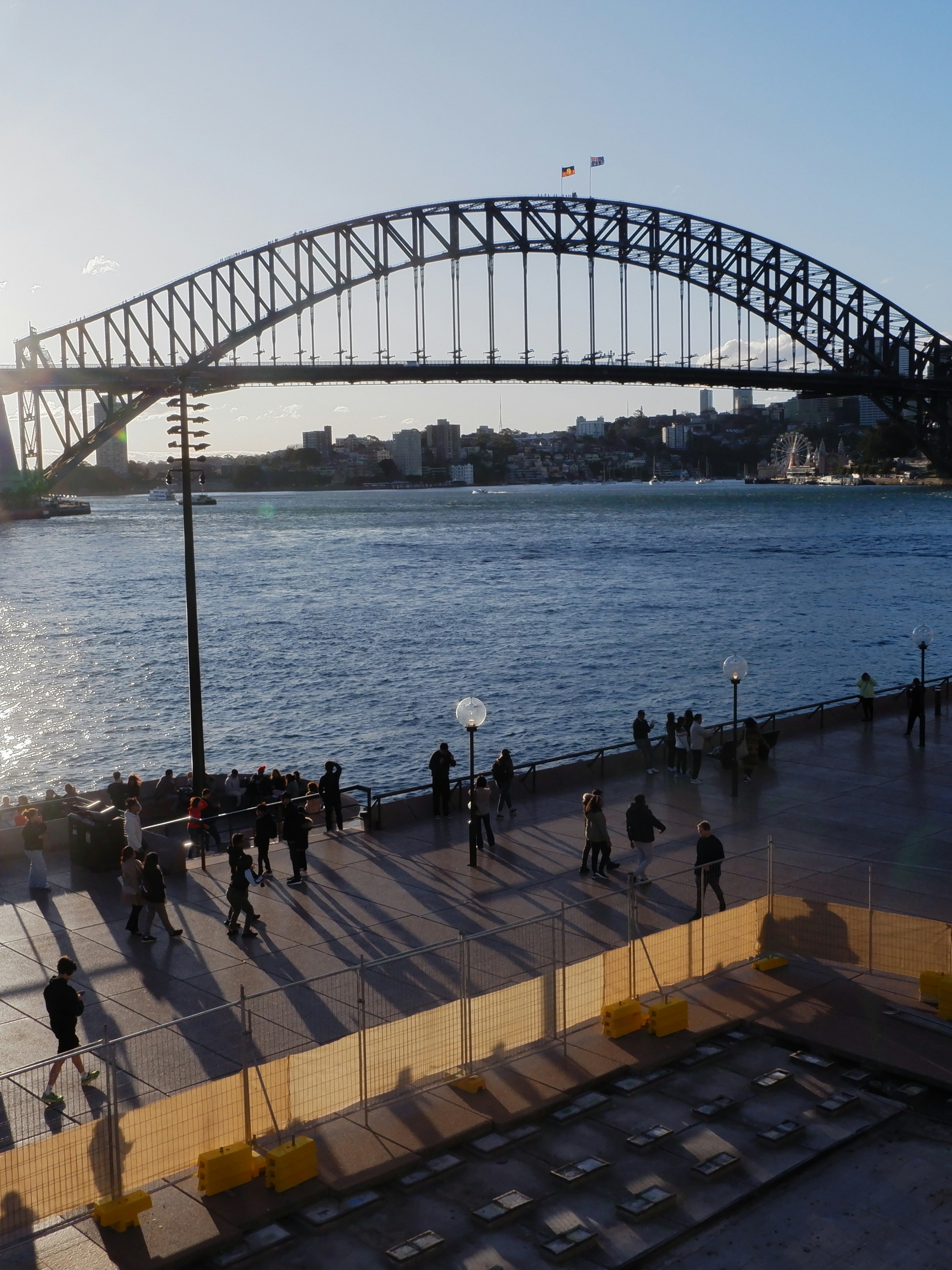 a group of people walking along a pier next to a large bridge
