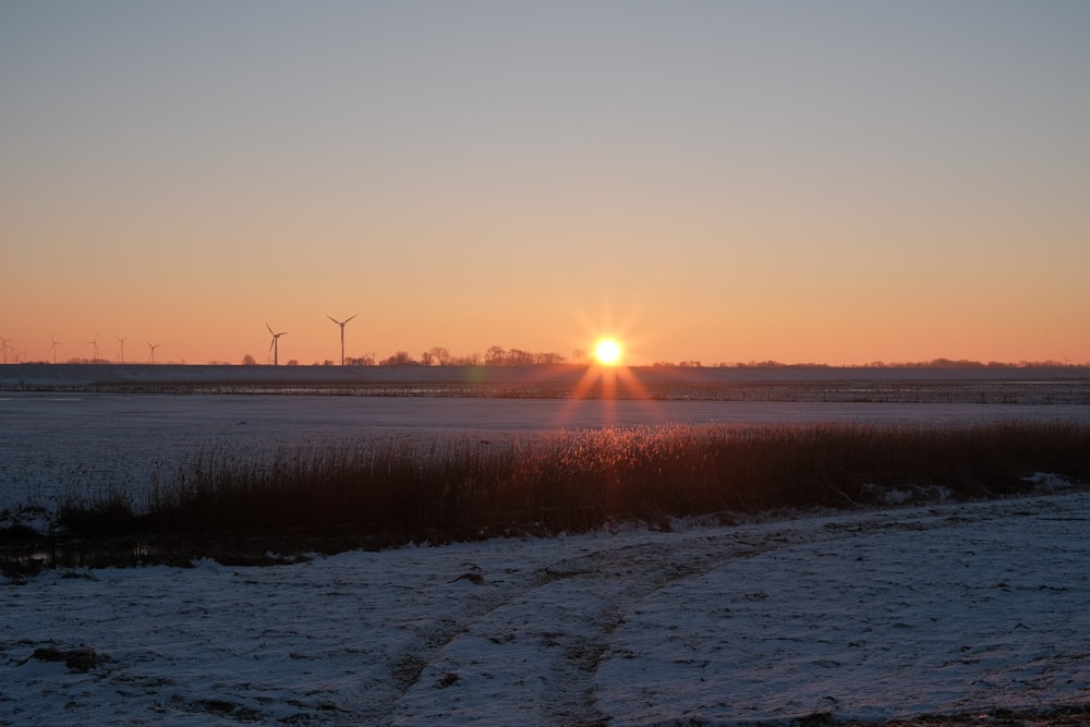 the sun is setting over a snowy field