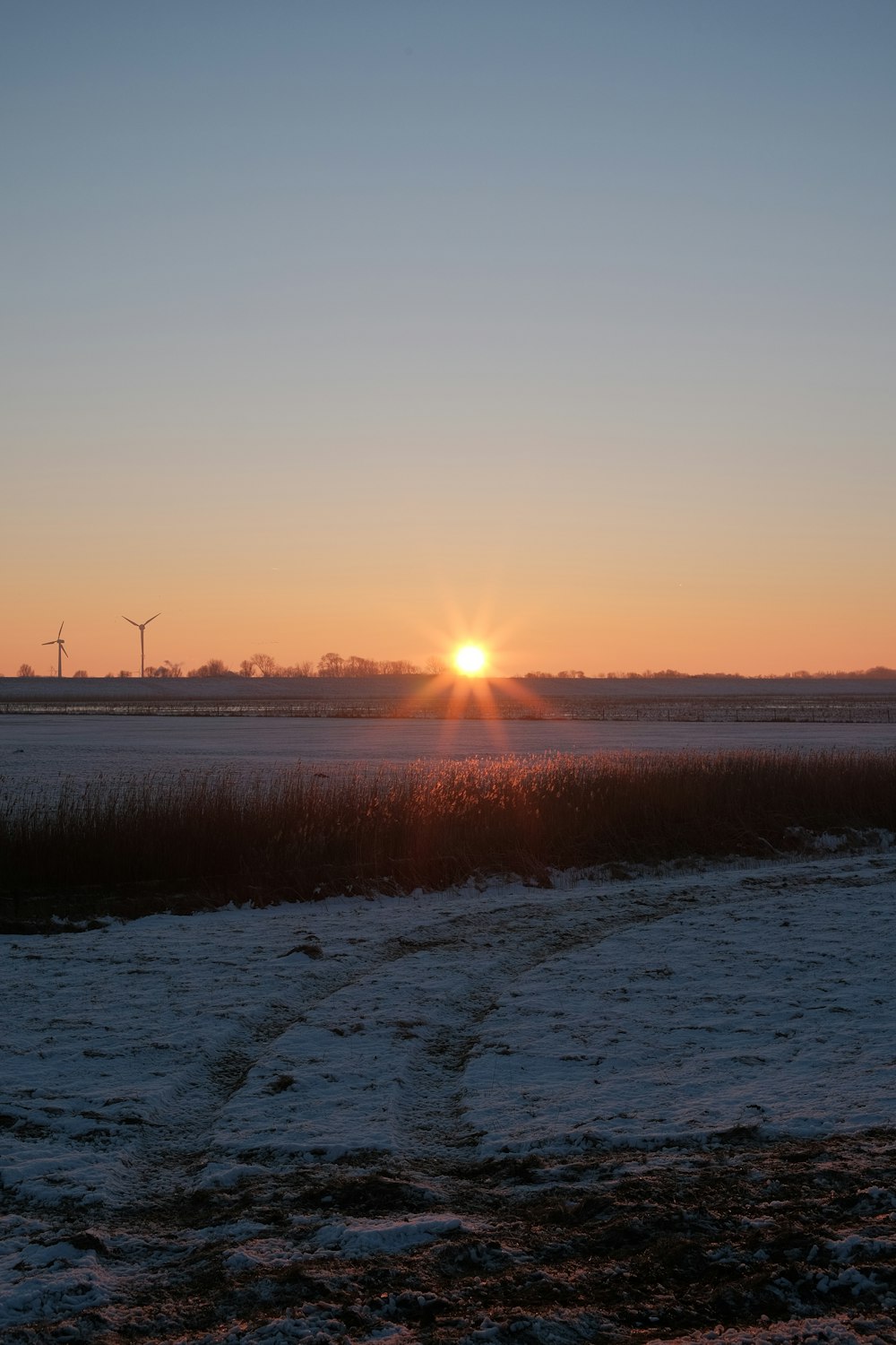 the sun is setting over a snowy field