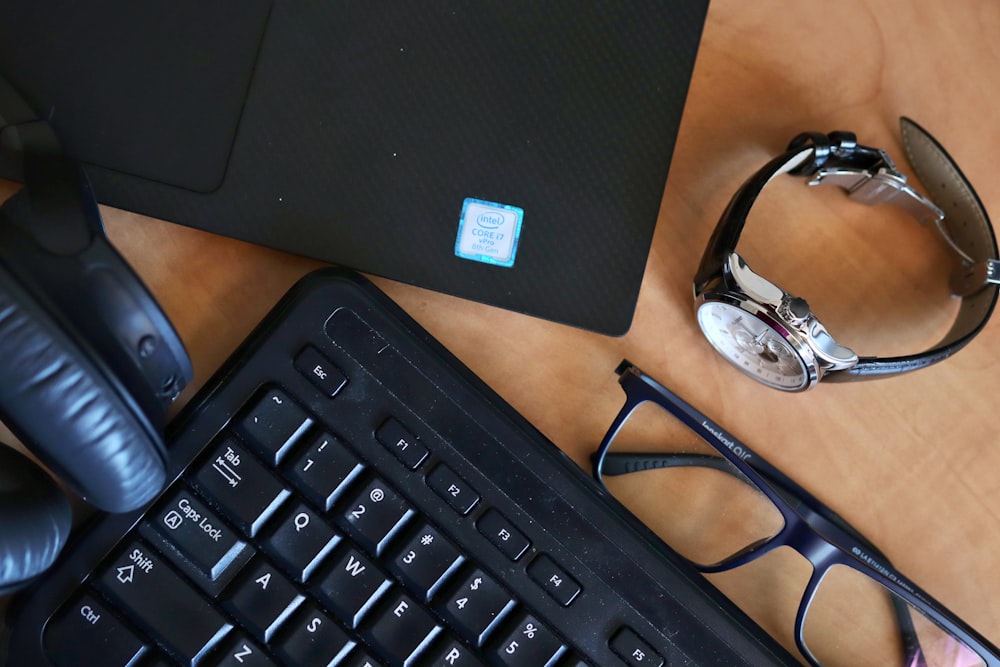 a desk with a keyboard, glasses and a laptop