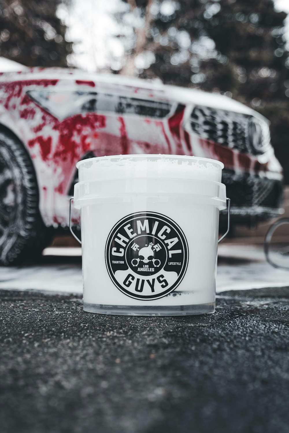 a bucket of paint sitting in front of a red car