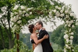 a bride and groom kissing under a floral arch