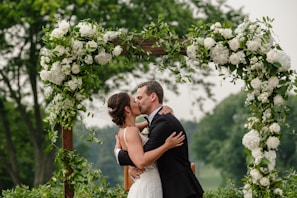 a bride and groom kissing under a floral arch