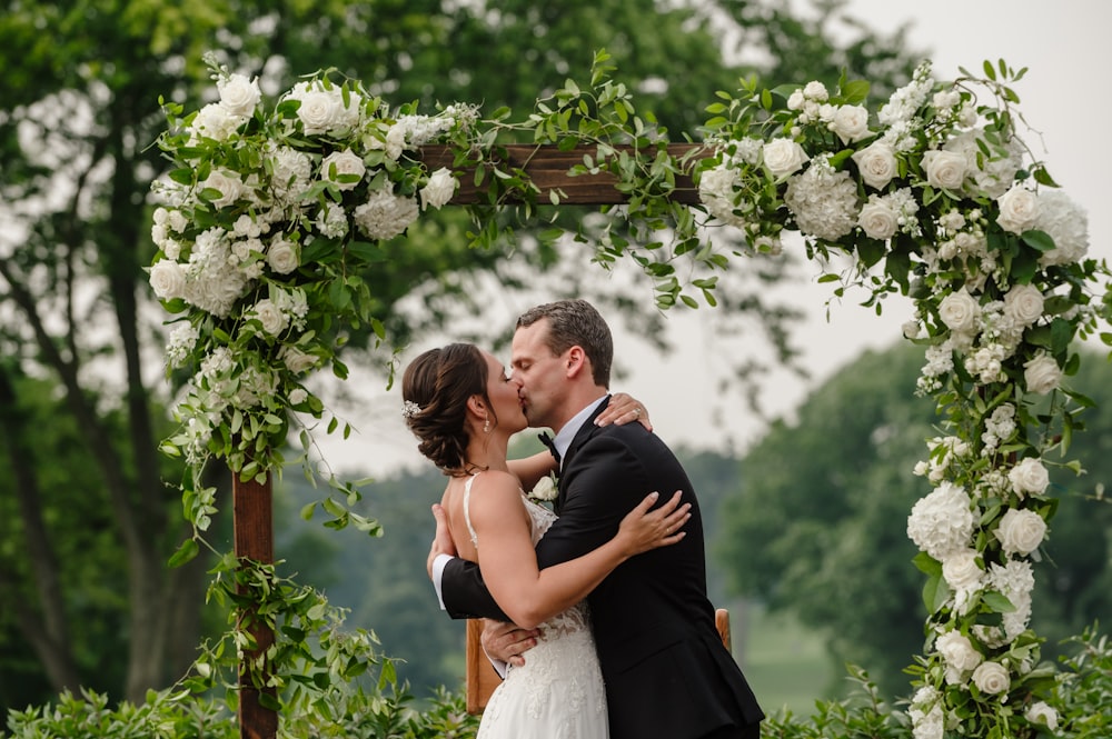 a bride and groom kissing under a floral arch