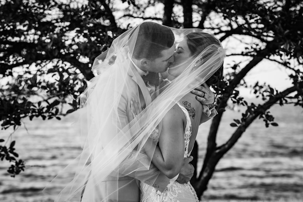 a bride and groom kissing under a tree