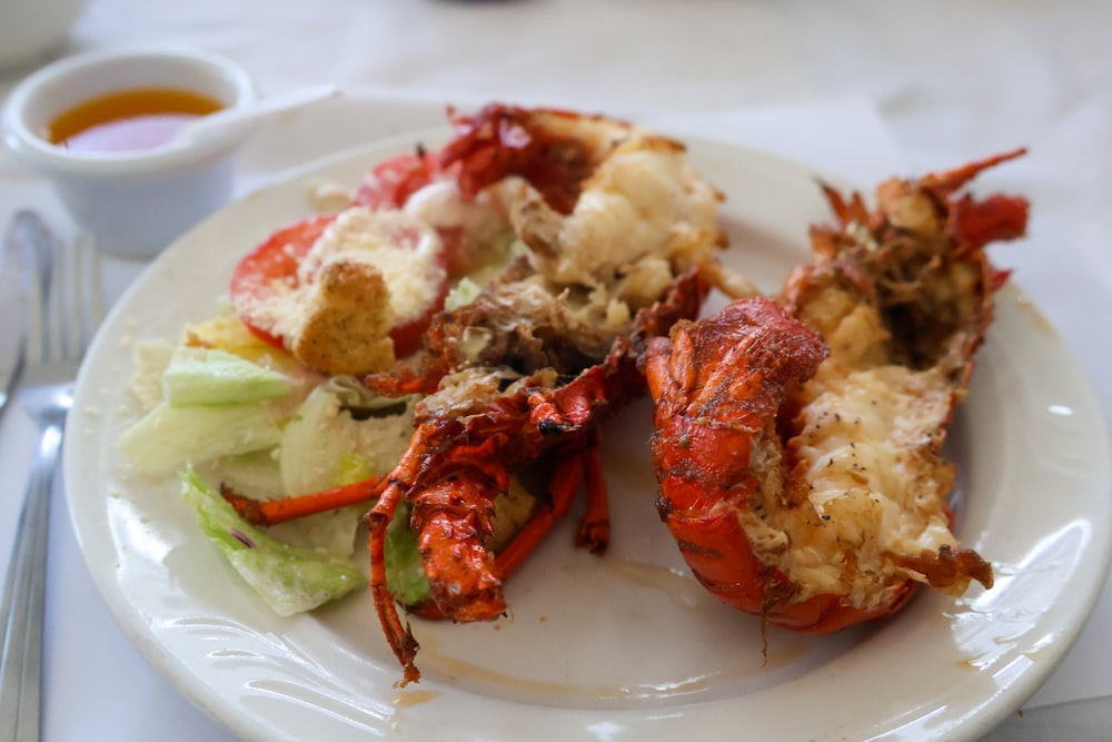 a white plate topped with lobster next to a salad