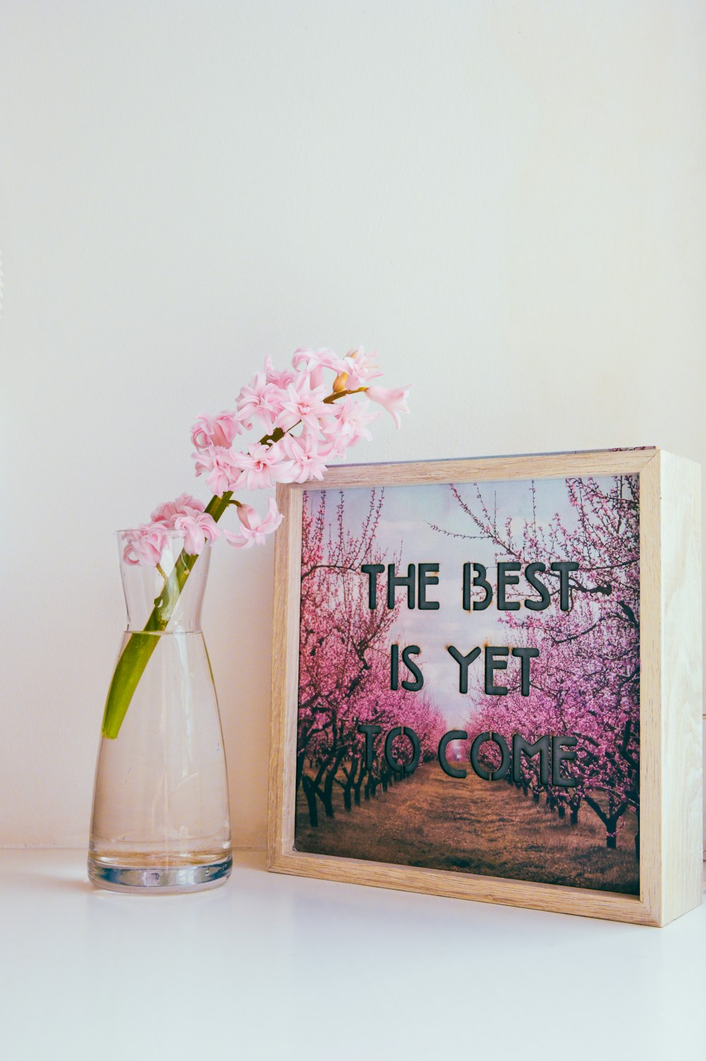 a vase with pink flowers sitting next to a picture frame