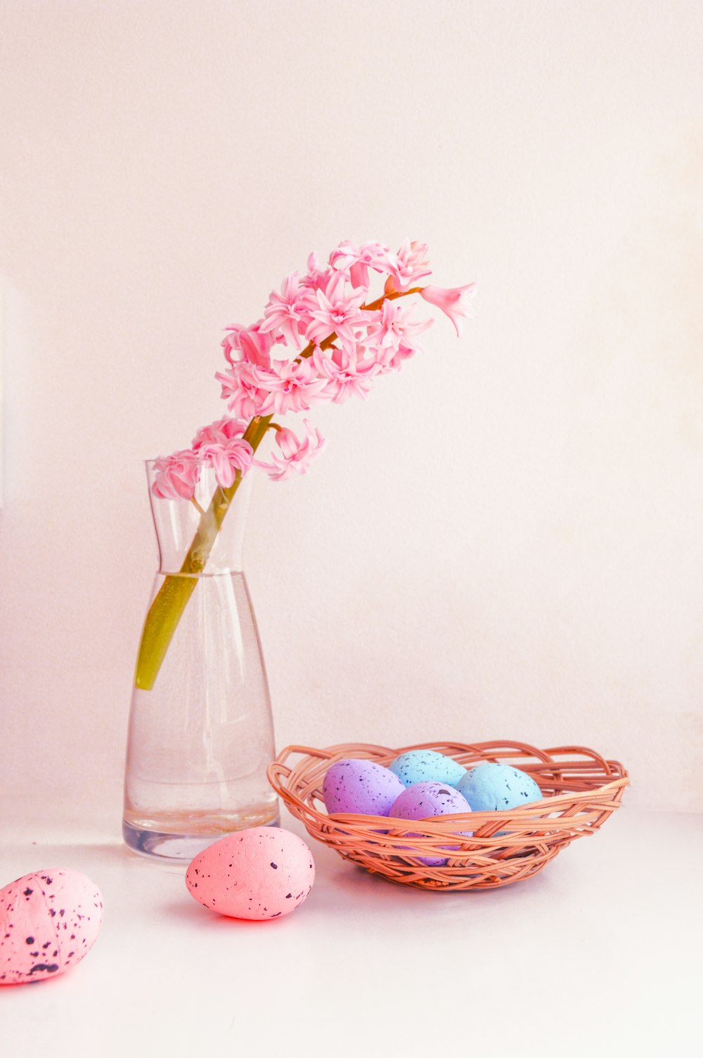 a vase filled with pink flowers next to a basket of eggs